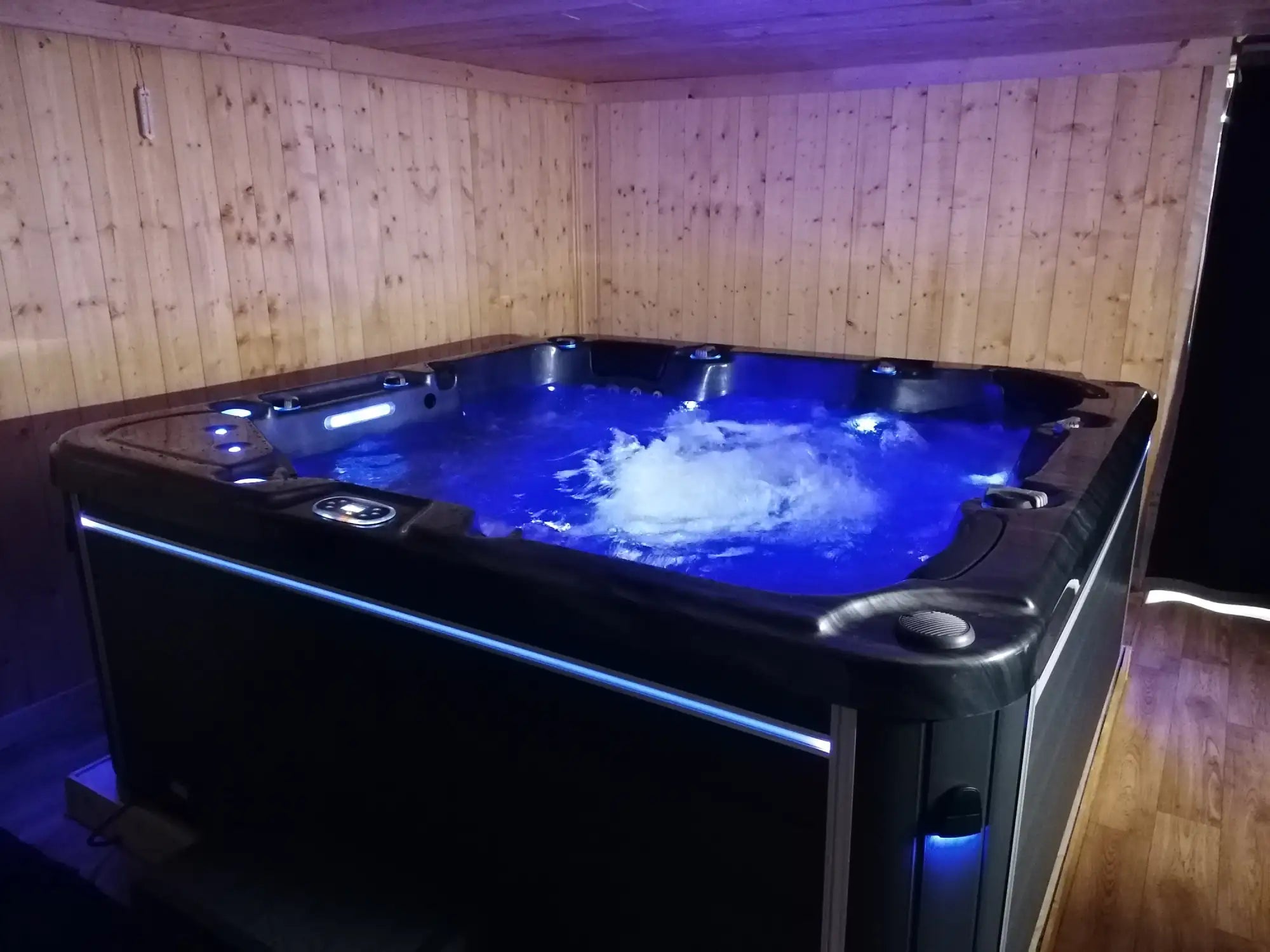 Baignoire à remous noire avec éclairage LED bleu et eau bouillonnante.