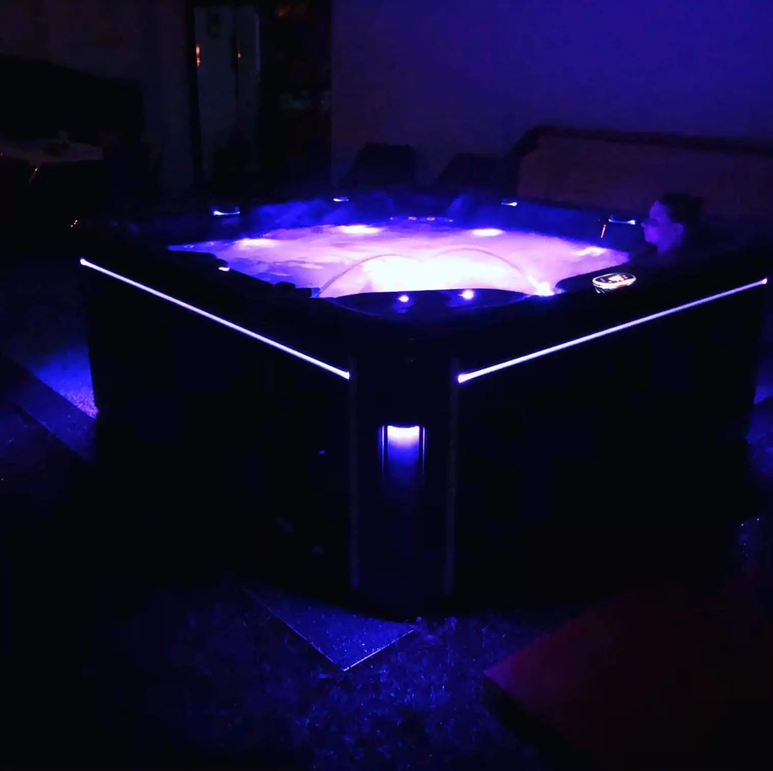 Baignoire à remous noire avec des lumières LED bleues luminescentes soulignant ses bords et illuminant l'eau bouillonnante à l'intérieur.