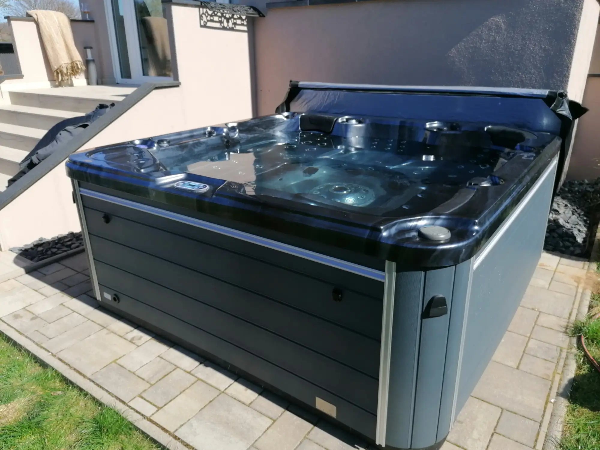 Bain à remous noir et gris avec un design élégant et moderne présentant des courbes fluides et des panneaux de commande intégrés.